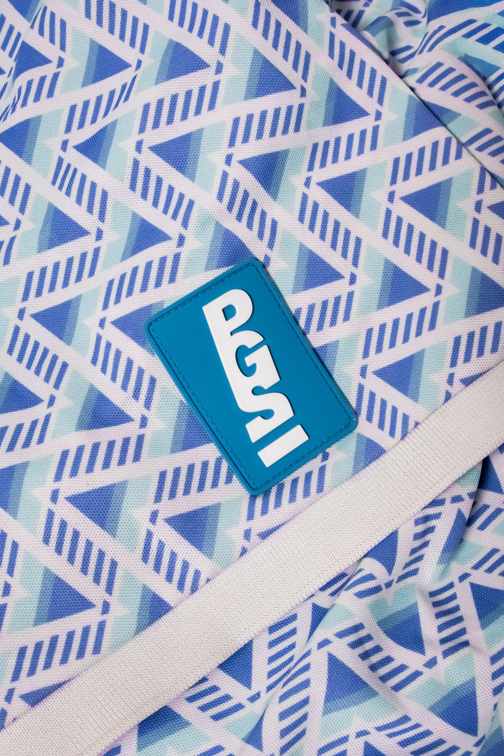 Sky Blue 90 Polo sleeve close-up showing the blue PGS patch, geometric print, and white cuff.